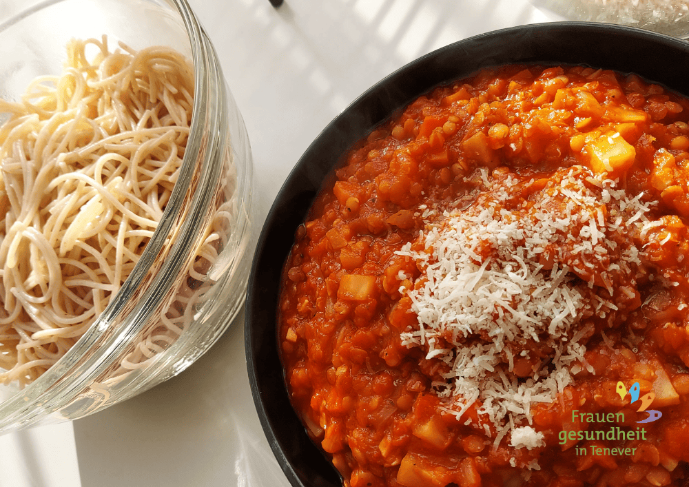 In der linken Schüssel sind Vollkornspaghetti und rechts eine Linsenbolognese mit Parmesan.